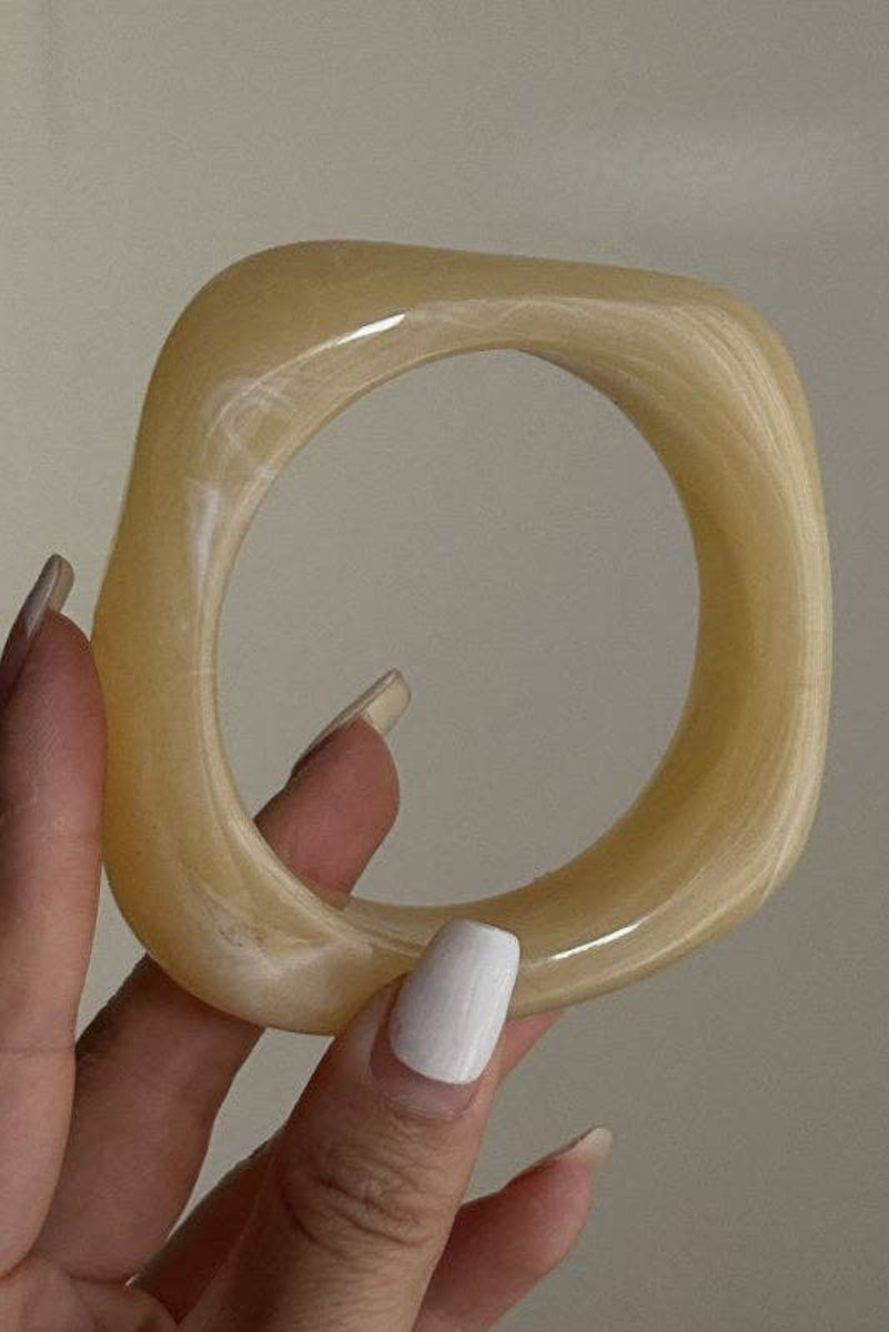 Hand holding a square-shaped beige bracelet against a plain background