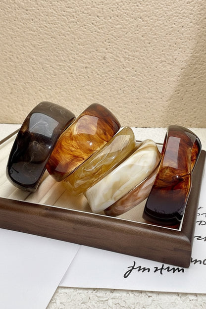 Set of four tortoiseshell bangles on a wooden tray with a neutral background