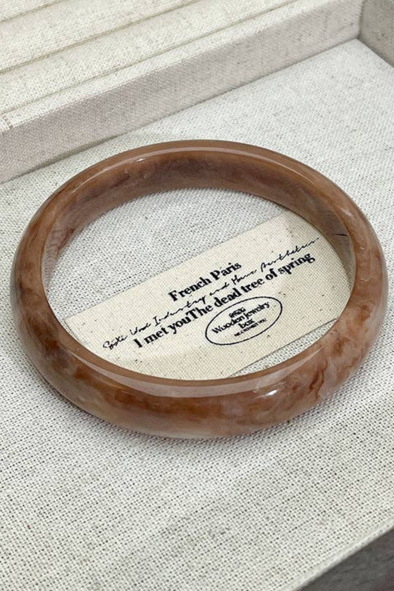 Brown bracelet on a textured fabric surface with a card underneath