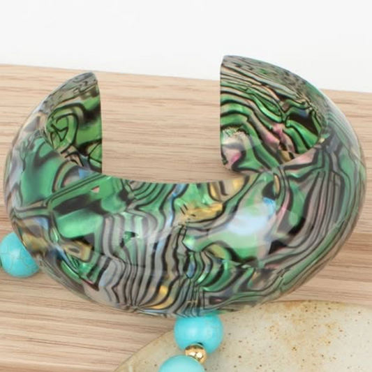 Green and gold patterned bracelet with turquoise beads on a wooden surface