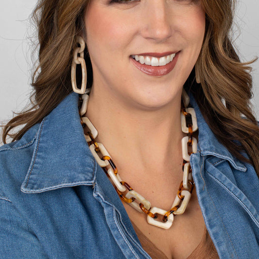 Woman wearing a tortoiseshell and cream necklace with a denim jacket on a plain background