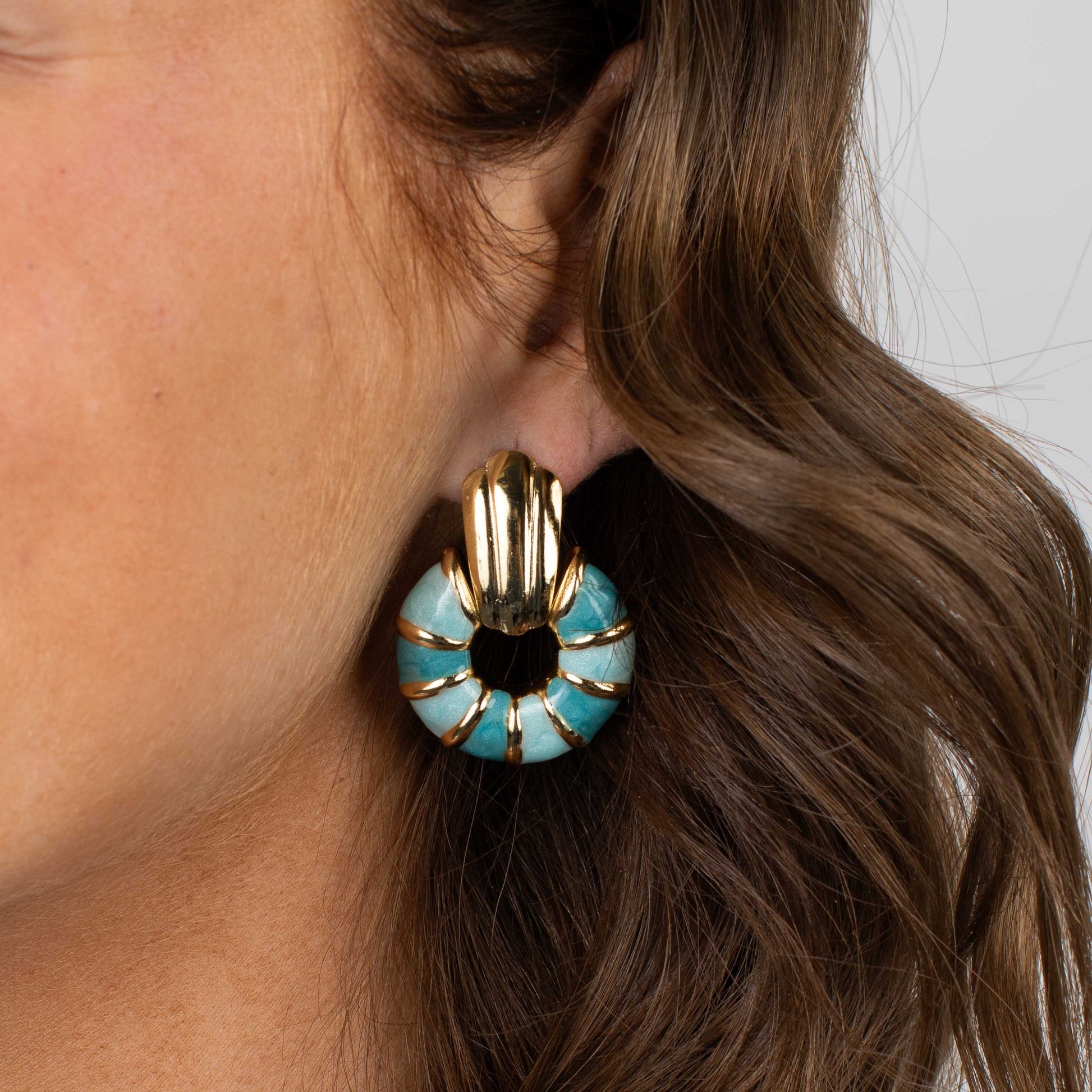 Close-up of a person wearing a turquoise and gold earring.