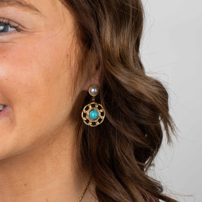 Close-up of a woman wearing a gold earring with a turquoise gemstone and pearl.