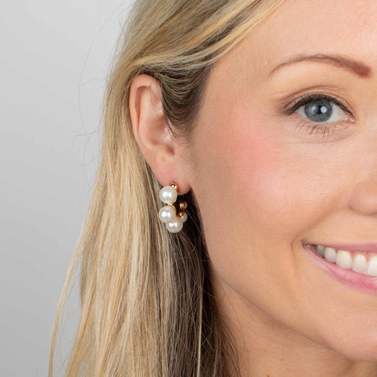 Close-up of a woman wearing pearl earrings with a plain background