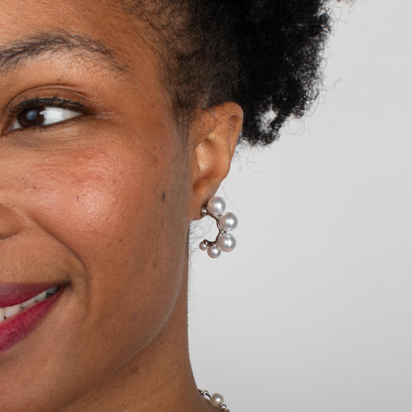 Close-up of a woman wearing pearl earrings with a plain background