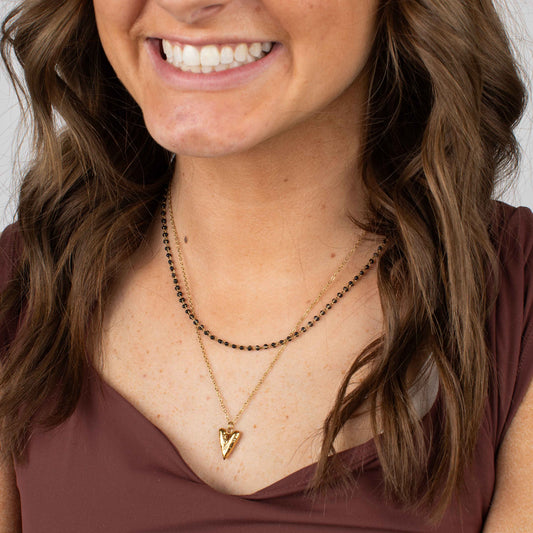 Woman wearing a gold necklace with an arrow pendant against a neutral background