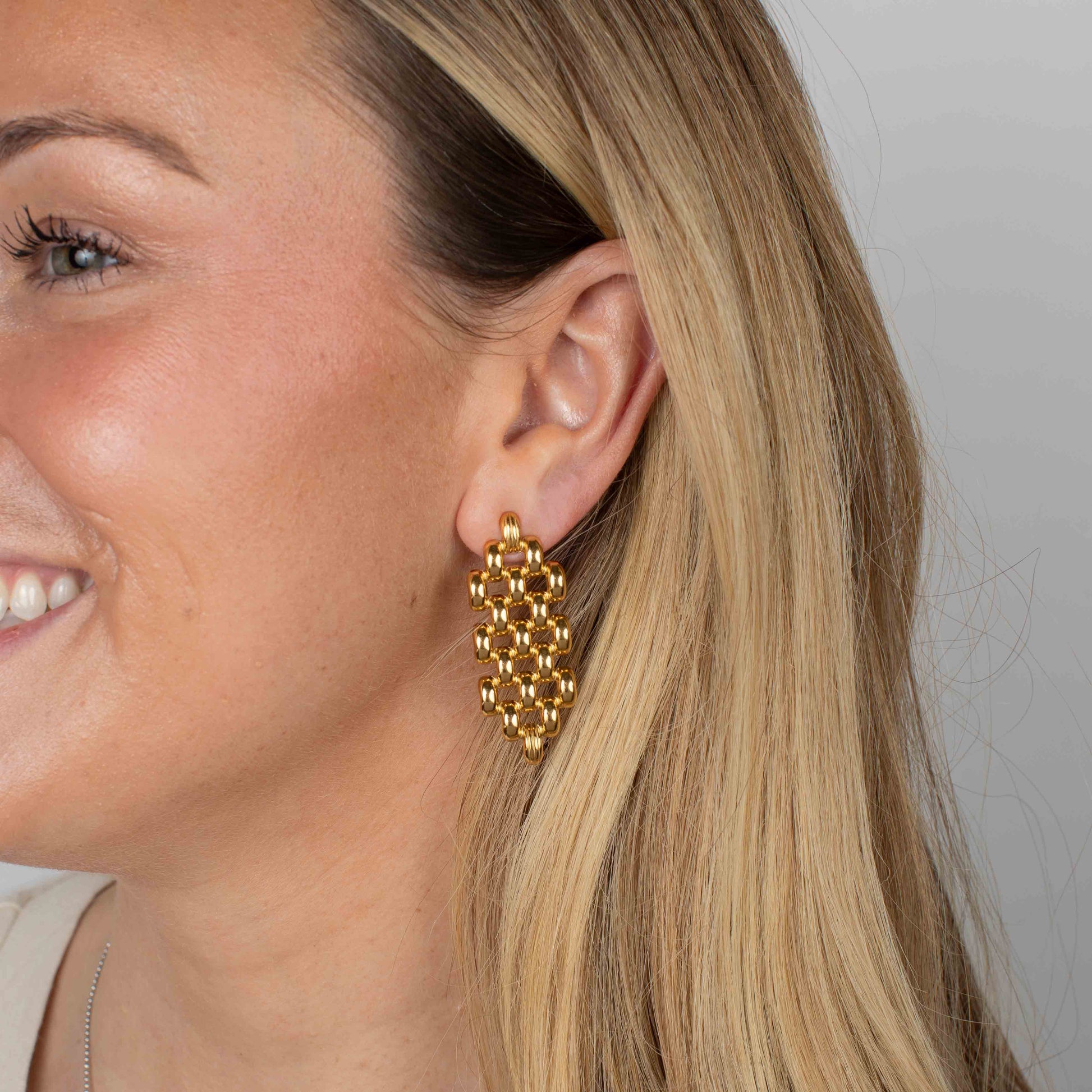 Close-up of a woman wearing gold earrings with a plain background