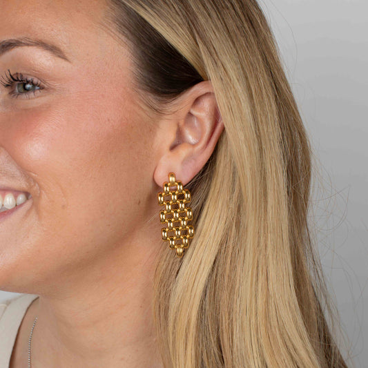 Close-up of a woman wearing gold earrings with a plain background