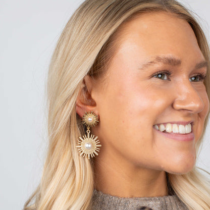 Woman wearing gold earrings with a pearl center against a plain background