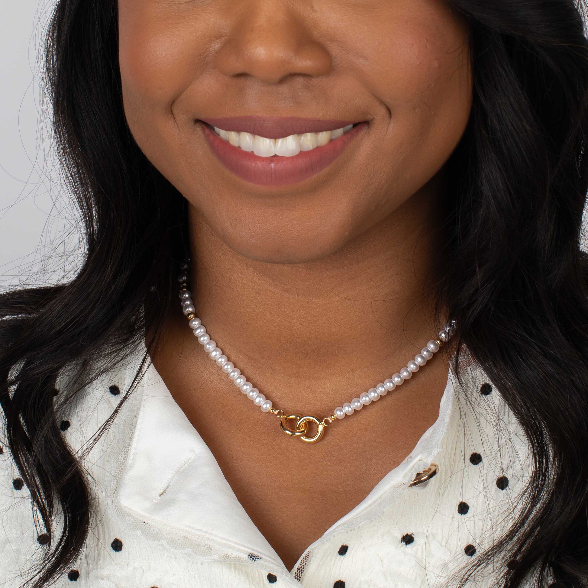 Woman wearing a pearl necklace with a gold clasp against a neutral background