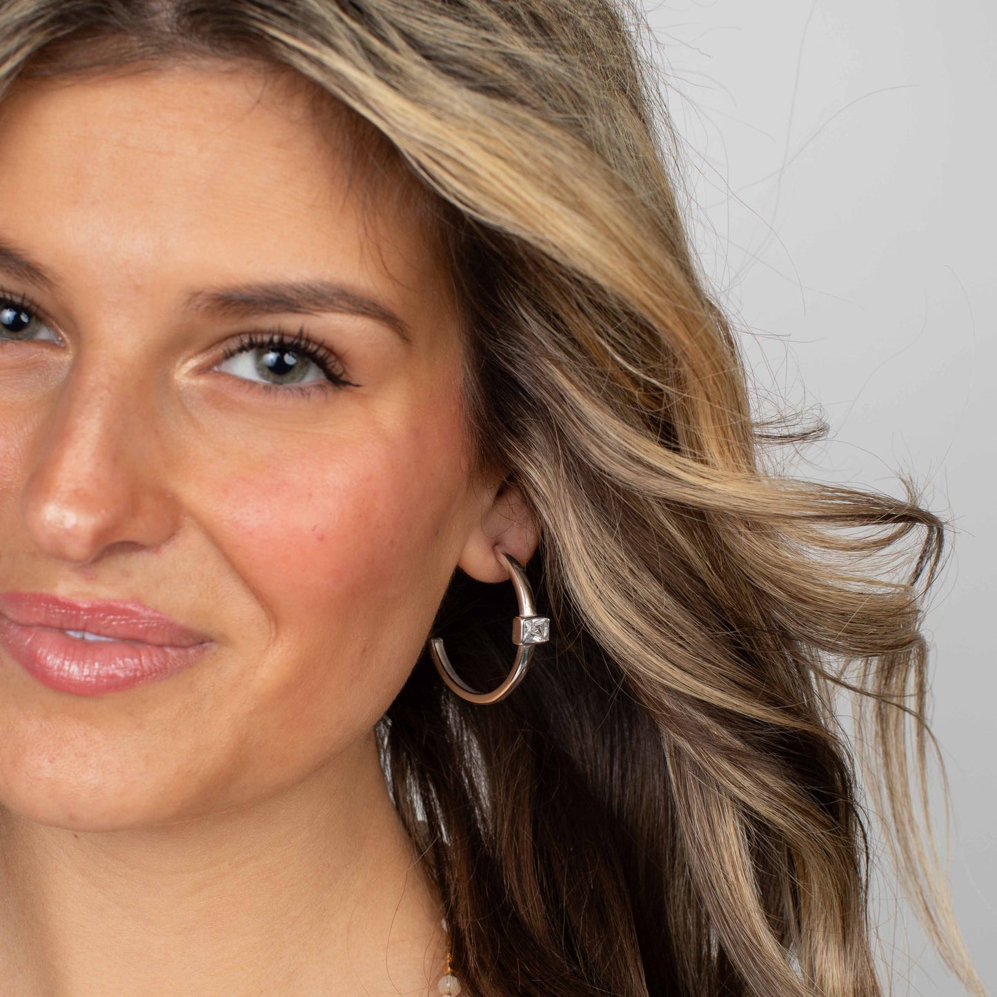 Close-up of a woman wearing silver hoop earrings with a neutral background