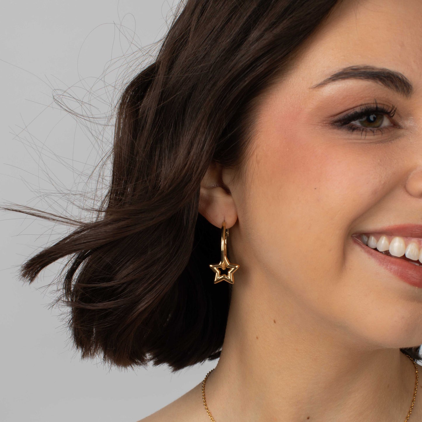 Close-up of a woman wearing gold star-shaped earrings against a neutral background
