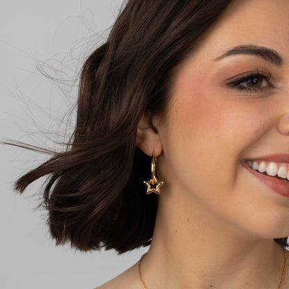 Close-up of a woman wearing gold star-shaped earrings against a neutral background
