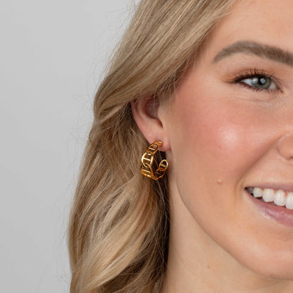 Close-up of a woman wearing gold hoop earrings with a plain background