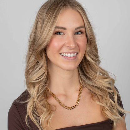Woman wearing a gold necklace against a plain background