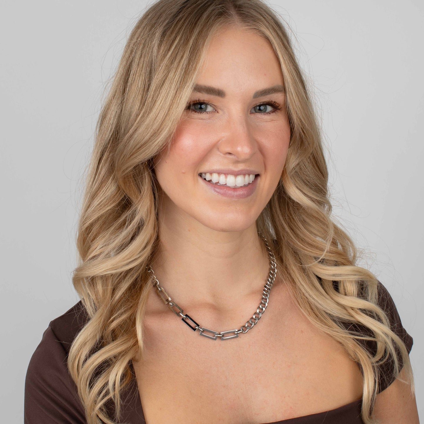 Woman wearing a silver chain necklace against a plain background