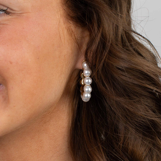 Close-up of a woman wearing pearl earrings with a neutral background