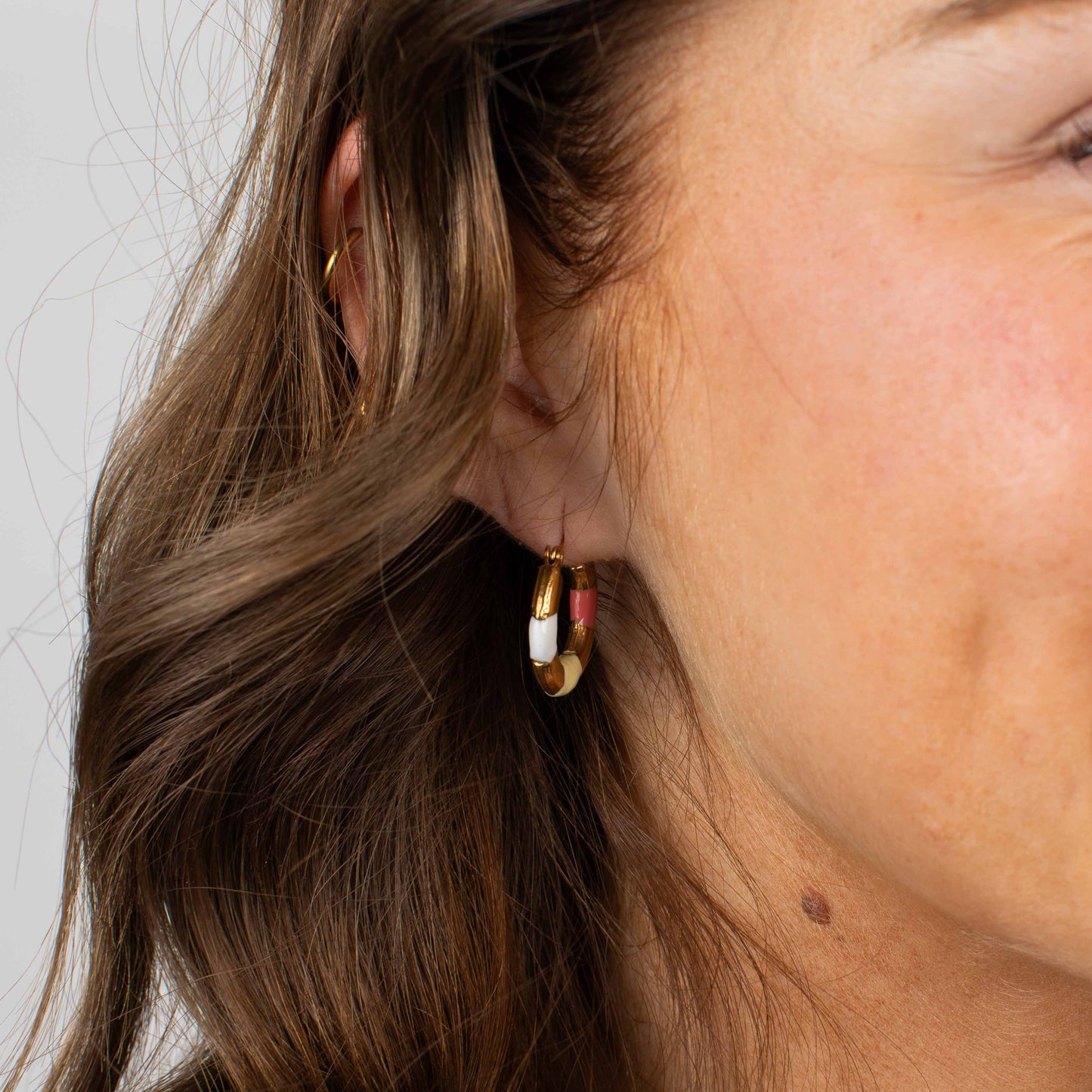 Close-up of a person wearing gold hoop earrings with colorful stones on a neutral background
