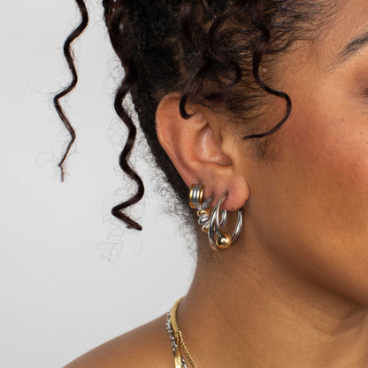 Close-up of an ear wearing gold hoop earrings with a neutral background