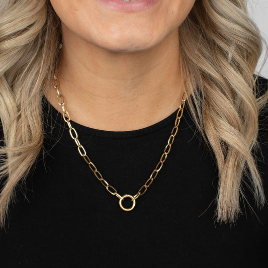 Gold chain necklace worn by a person with blonde hair against a black background