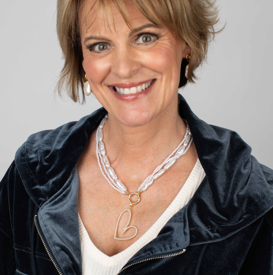 Woman wearing a necklace with a heart pendant against a gray background