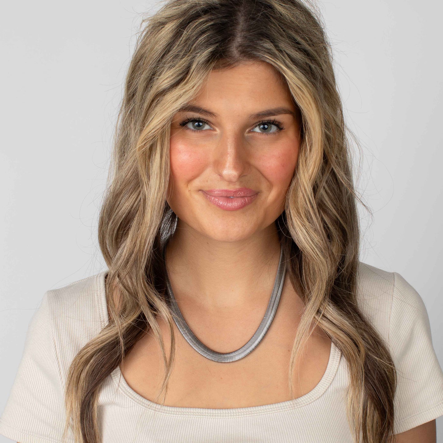 Woman with long, wavy hair wearing a necklace against a plain background