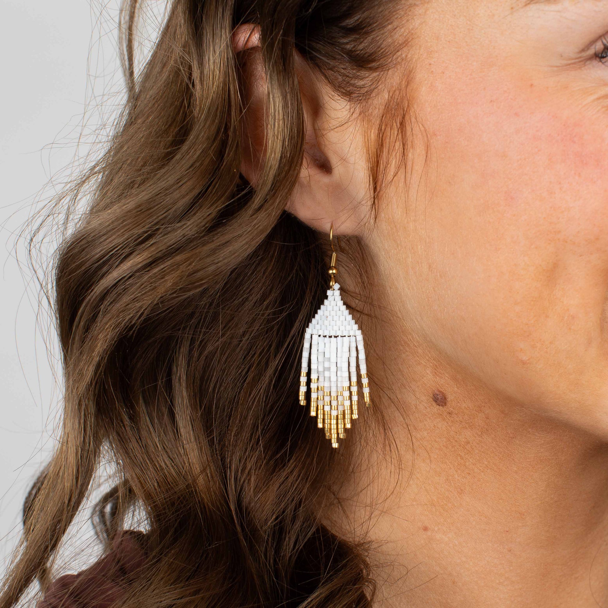 Close-up of a woman wearing a beaded earring with a plain background