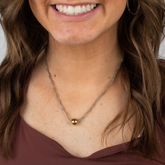 Close-up of a woman wearing a gold necklace with a brown background