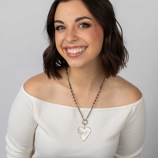 Woman wearing a white off-shoulder top and a necklace with a heart pendant against a plain background