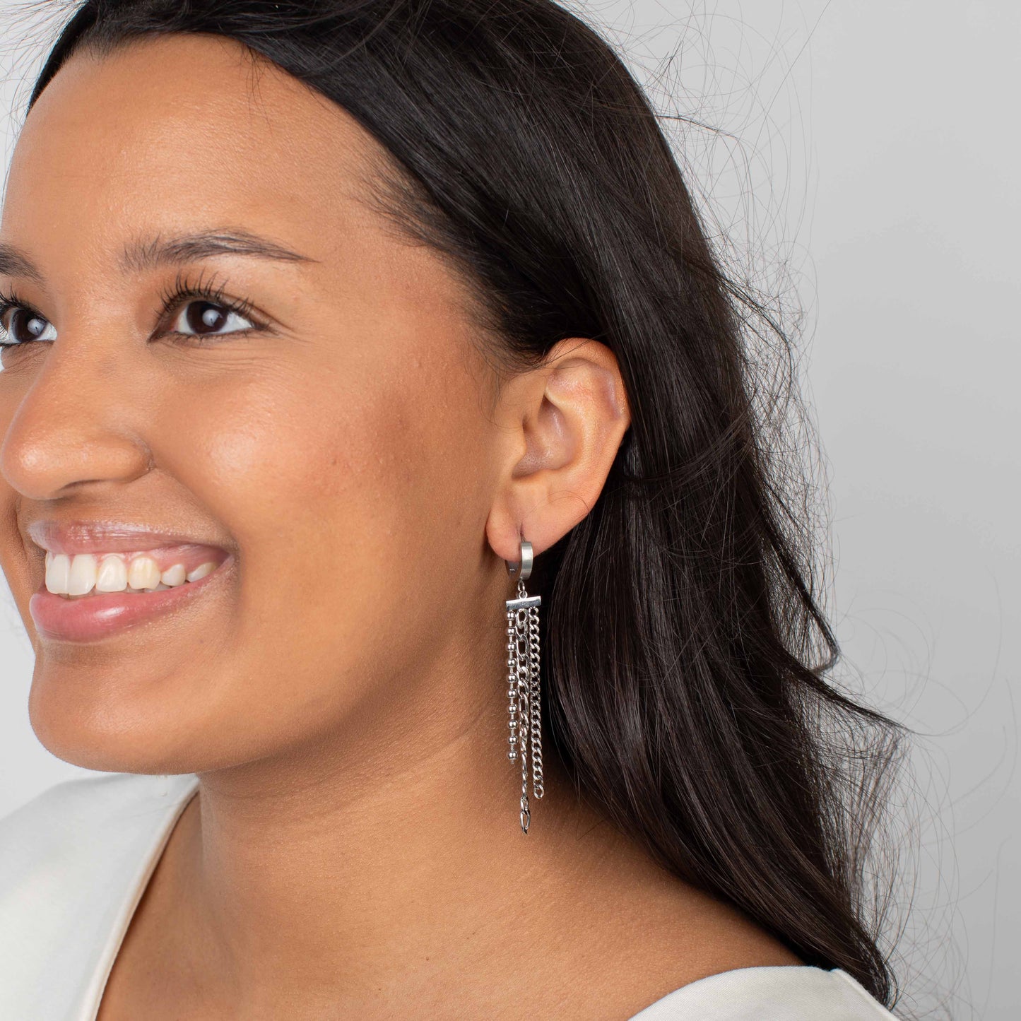 Woman wearing a silver earring with tassels on a plain background