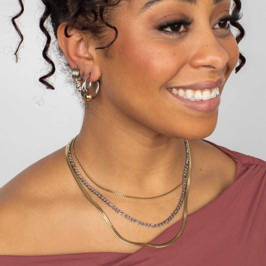 Woman wearing multiple necklaces and hoop earrings against a neutral background