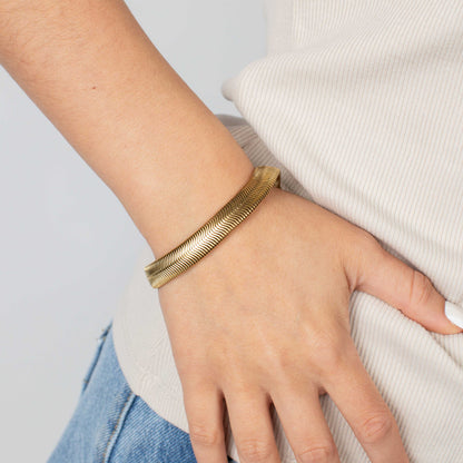 Gold bracelet on a wrist with a neutral background