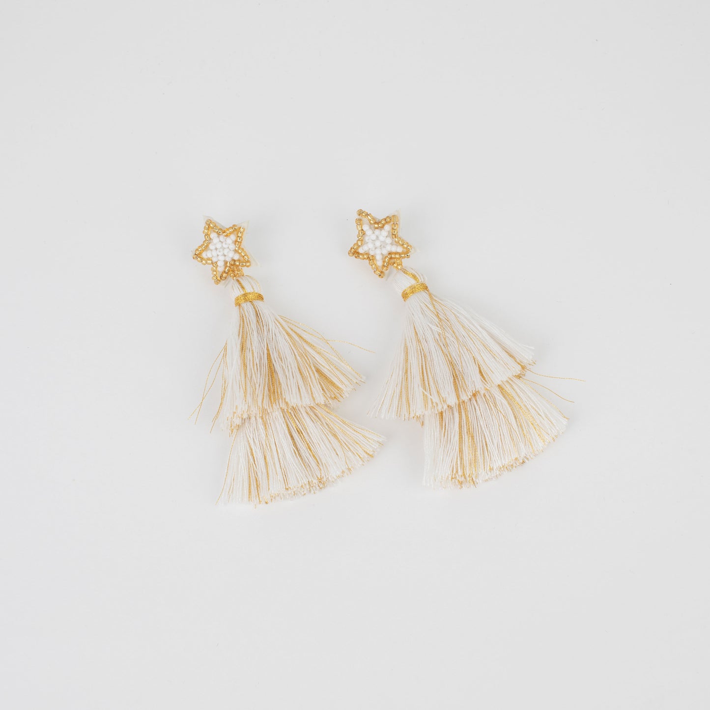 Gold tassel earrings with star-shaped top on a light gray background