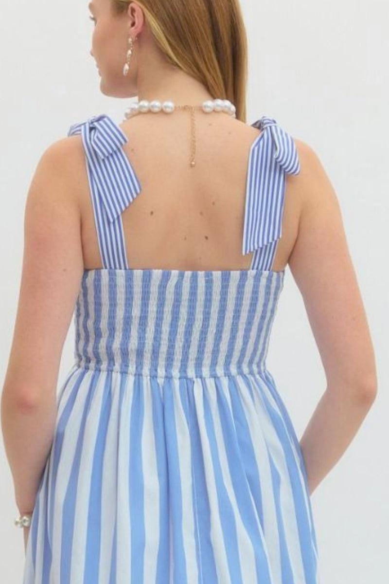 Woman wearing a blue and white striped dress with bow straps on a plain background