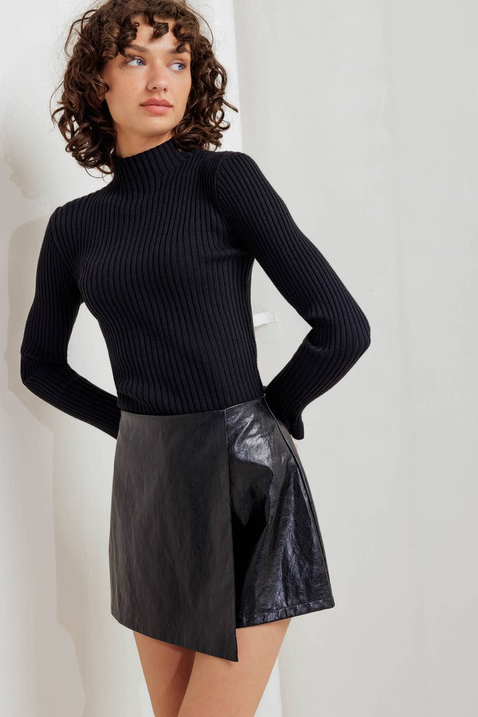 Woman wearing a black ribbed turtleneck sweater and black leather skirt against a white background
