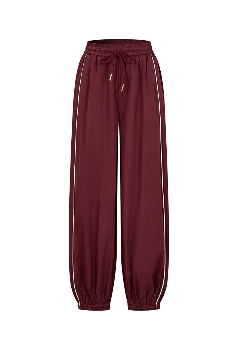 A pair of relaxed-fit jogger pants in a deep burgundy color, featuring white stripes down the sides and a matching drawstring waistband, shown against a plain white background.