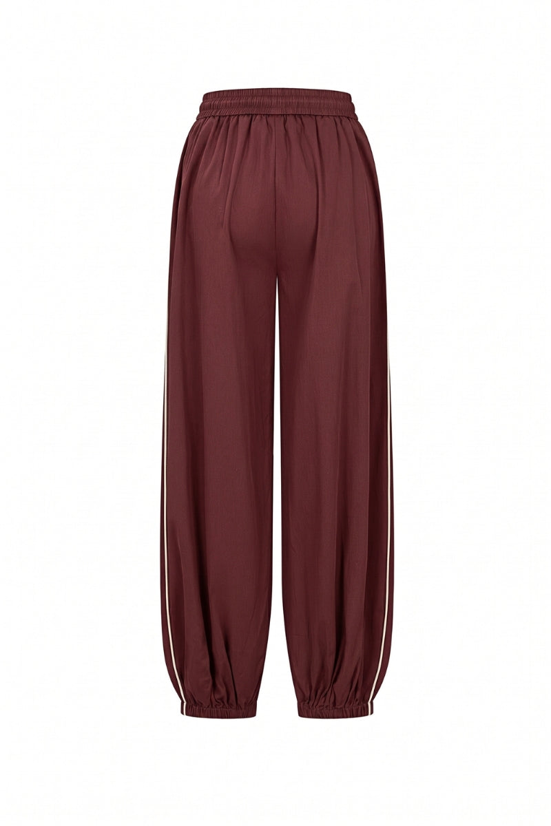 A pair of loose-fitting jogger-style pants in a deep burgundy or maroon color, featuring white side stripes down the legs and elastic cuffs, shown against a plain white background.