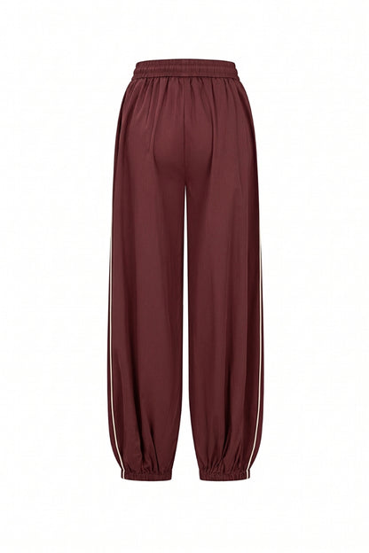 A pair of loose-fitting jogger-style pants in a deep burgundy or maroon color, featuring white side stripes down the legs and elastic cuffs, shown against a plain white background.
