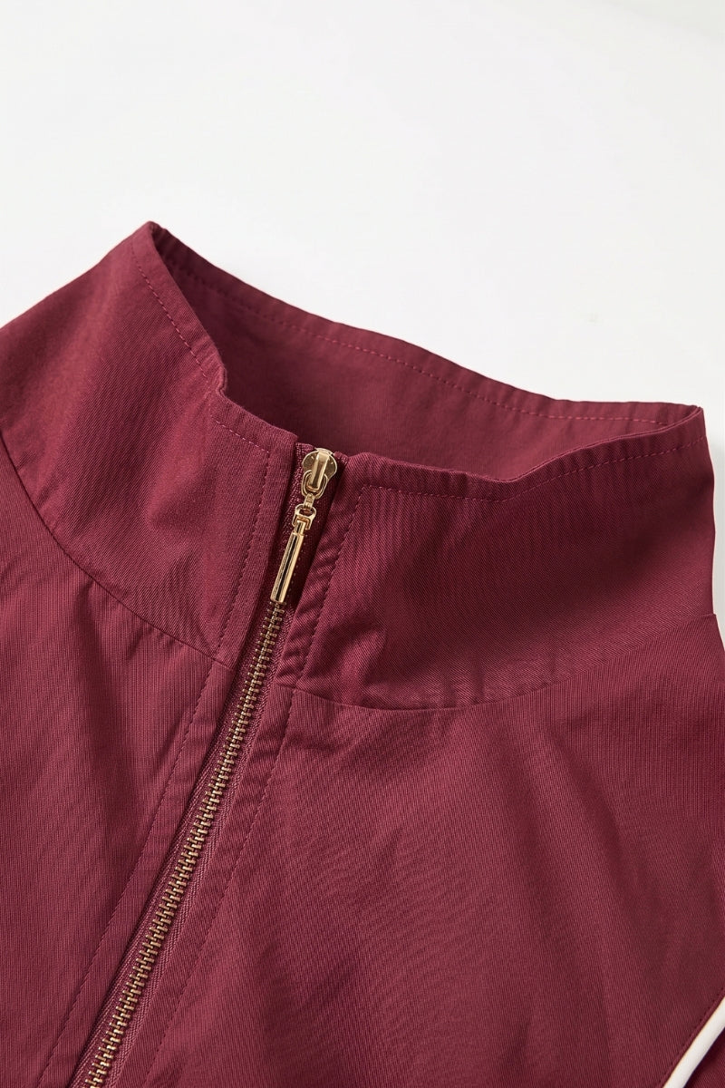 Close-up of a burgundy zip-up jacket with a high stand-up collar and a gold zipper, shown against a plain white background.