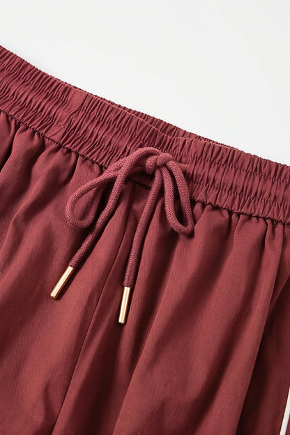 Close-up of a pair of dusty rose or burgundy drawstring shorts with gold-toned metal tips on the elastic cord, set against a plain light background.