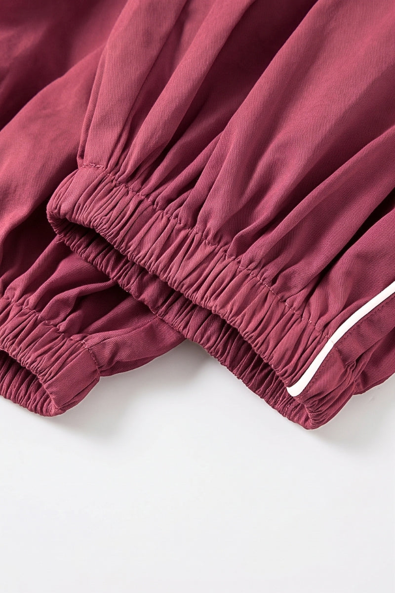 Close-up of a dusty rose or mauve-colored fabric garment, showing an elasticized gathered cuff with a thin white piping accent, laid flat on a white surface.