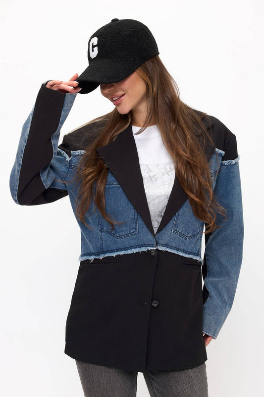 Woman wearing a black and denim jacket with a white shirt underneath, on a plain background
