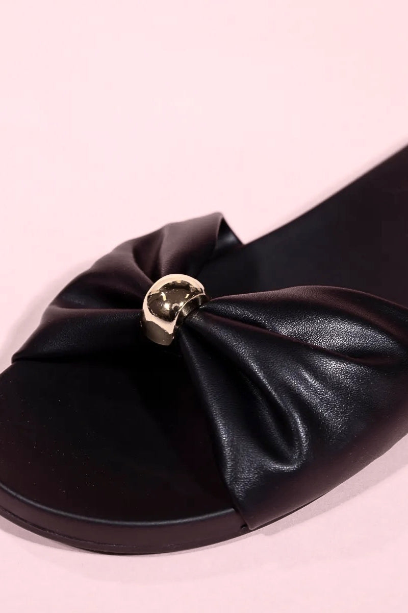 Black sandal with a large bow detail on a pink background