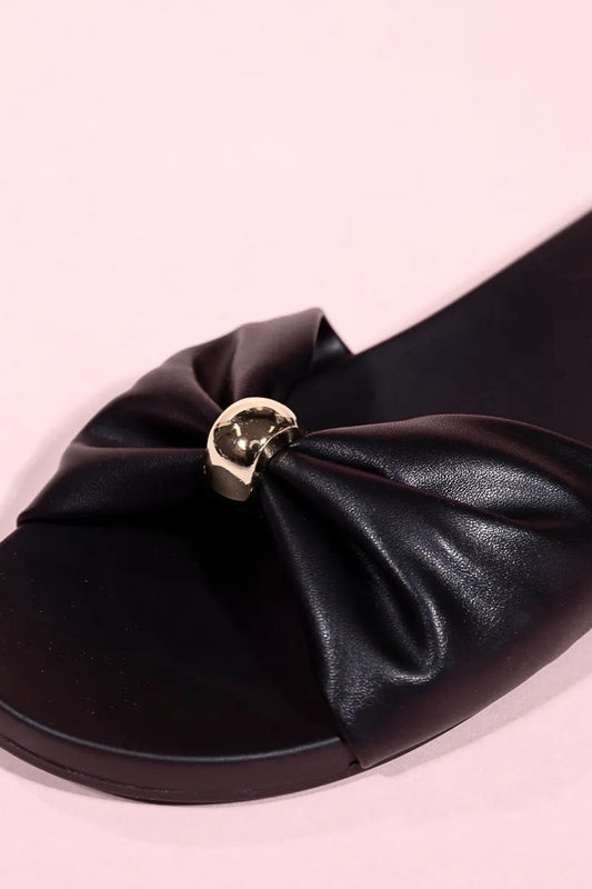 Black sandal with a large bow detail on a pink background