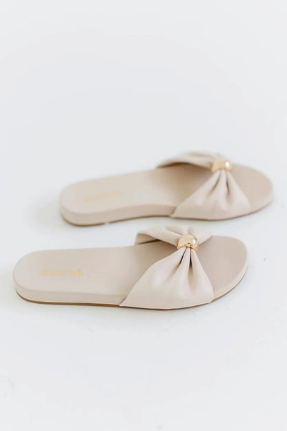 Pair of beige sandals with bow details on a light gray background