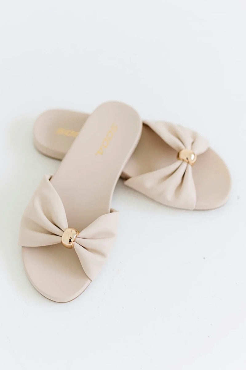 Beige slippers with bow details on a white background