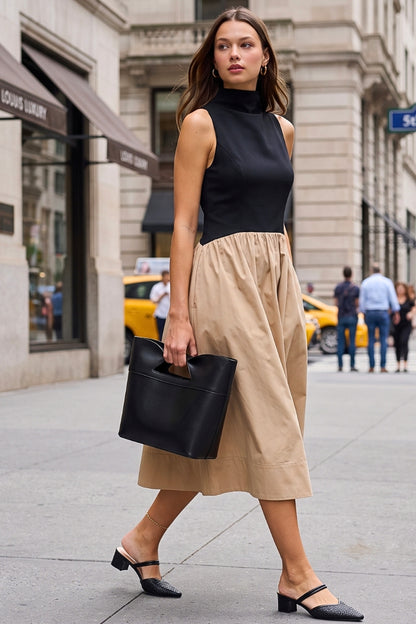 A woman walking on a city street wearing a sleeveless black mock-neck top and a beige midi skirt, carrying a black leather bucket bag.