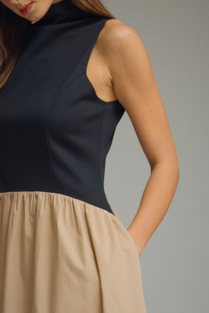 Woman wearing a black top and beige skirt against a gray background