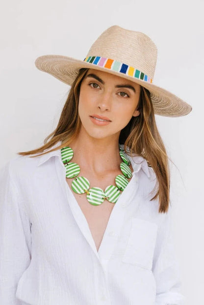 Woman wearing a straw hat with colorful band and green necklace against a white background