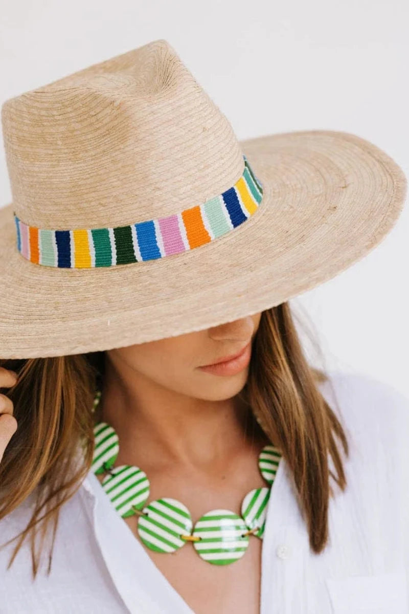 Woman wearing a straw hat with a colorful band and a green and white striped necklace on a light background